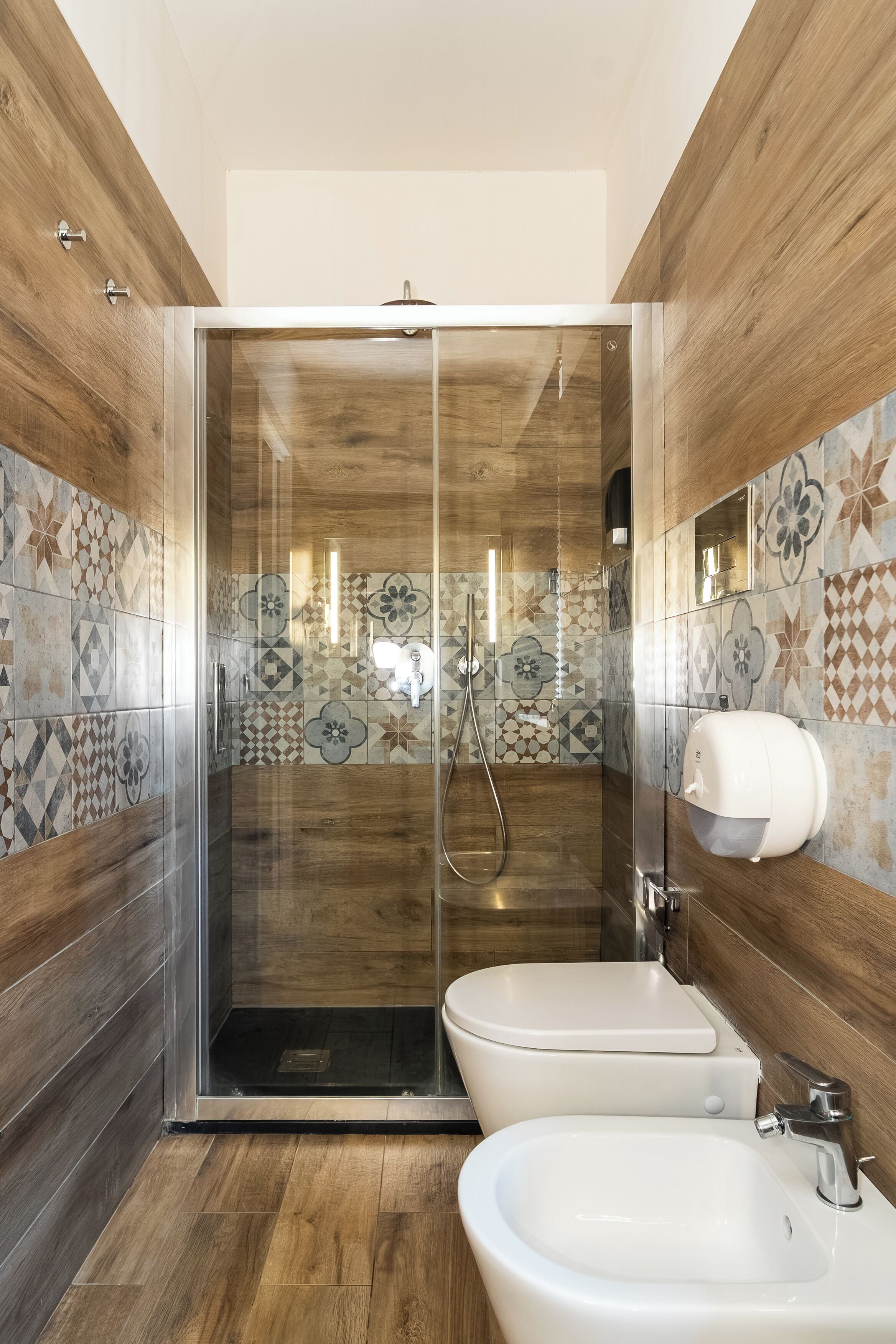 Ein modernes Badezimmer mit einer gläsernen Duschkabine, zwei Waschbecken und gemusterten Fliesen.