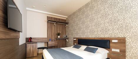A modern bedroom with a bed, bedside tables, a desk, and a TV mounted on the wall.