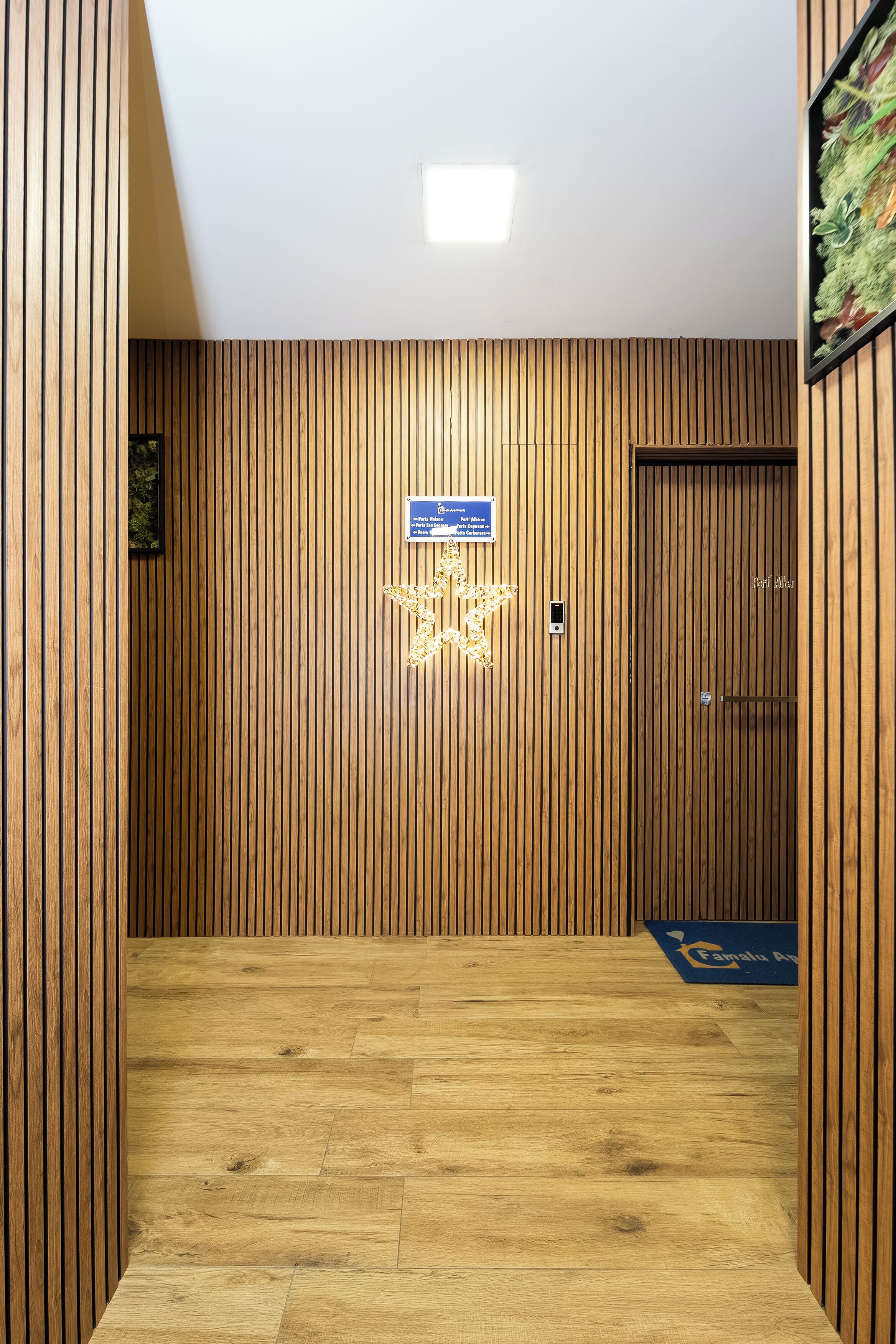 A wooden-paneled hallway with a star-shaped light fixture, a door with a sign, and a blue mat at the end.