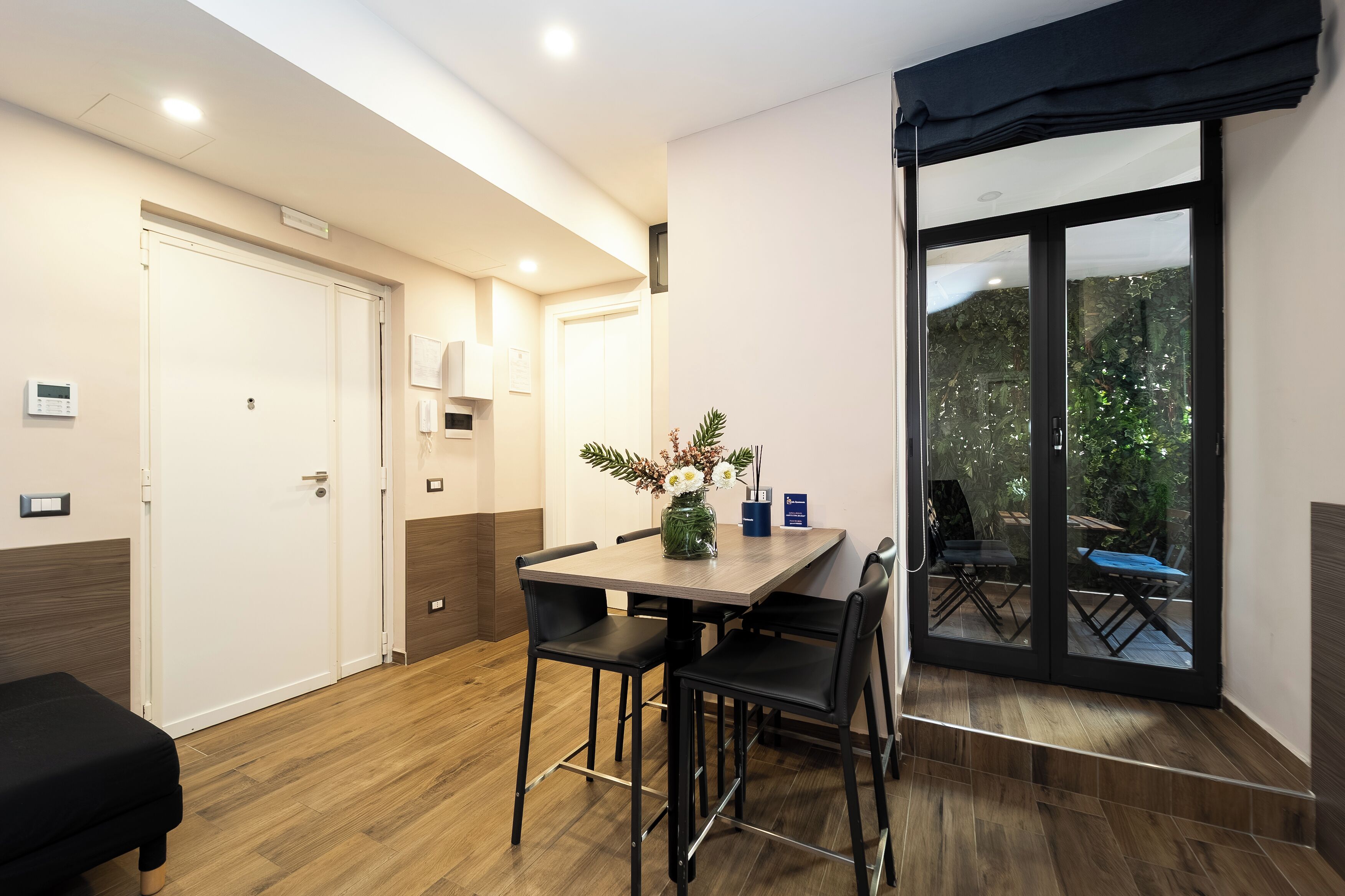 A modern dining area with a wooden table, black chairs, and a vase of flowers.