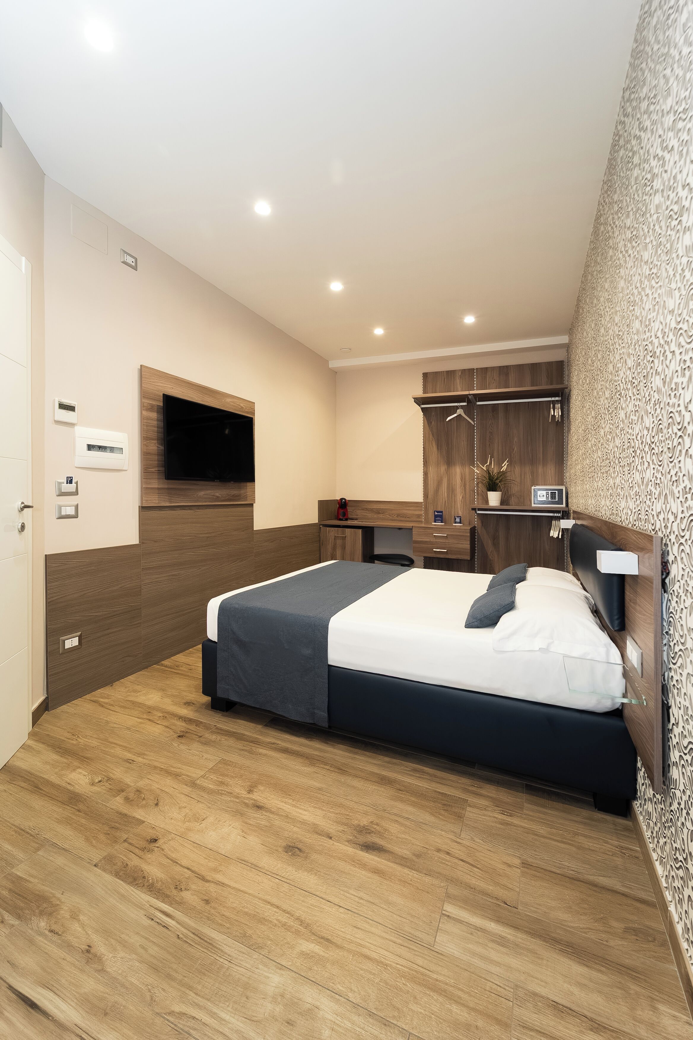 Ein modernes Hotelzimmer mit Bett, Schreibtisch, einem an der Wand befestigten Fernseher und einem Holzschrank.