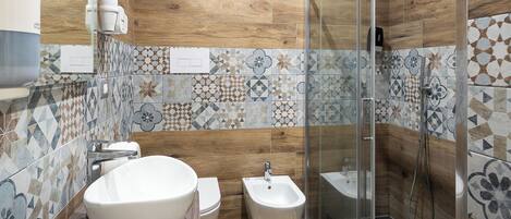A modern bathroom with a wooden vanity, a large sink, a toilet, a bidet, and a glass-enclosed shower area.