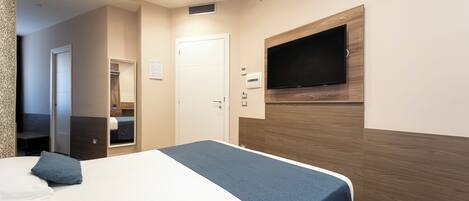 A hotel room with a bed, a television mounted on the wall, a door, and a small window.