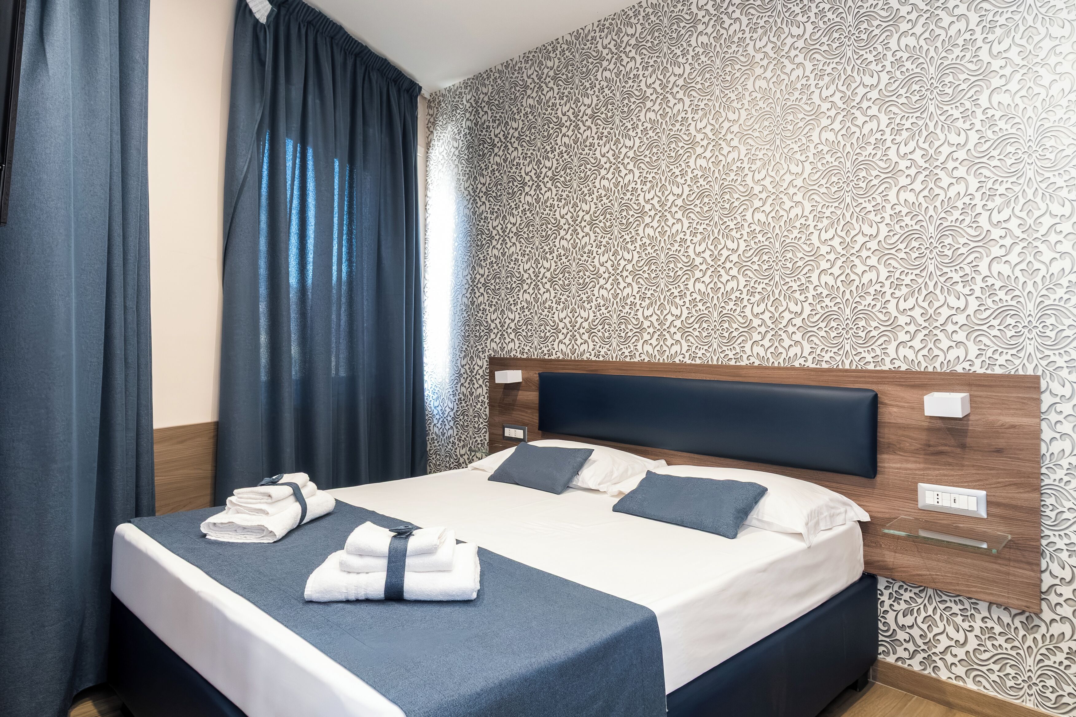 Ein Hotelzimmer mit einem ordentlich bezogenen Bett, einem Kopfteil und einer Wand mit Muster.