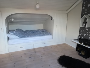 A compact room with a bed, a small desk, and a shelf with decorative items. - Rose Cottage 70m2 Tórshavn with Parking (Hoyvík)
