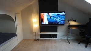 Un dormitorio con cama, escritorio, silla, televisor y lámpara.