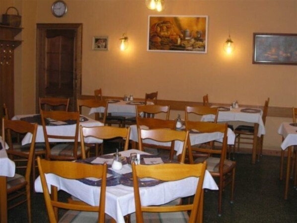 A dining area with multiple tables and chairs, a clock on the wall, and wall-mounted light fixtures. - Novomestsky Hotel (Prague)