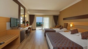 A hotel room with two beds, a desk, a TV, and a balcony with a view. - Telatiye Resort Hotel (Alanya)