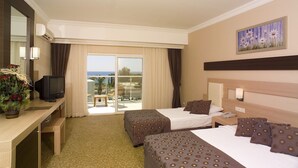 A hotel room with two beds, a desk with a TV, a balcony with a view, and a painting on the wall. - Telatiye Resort Hotel (Alanya)