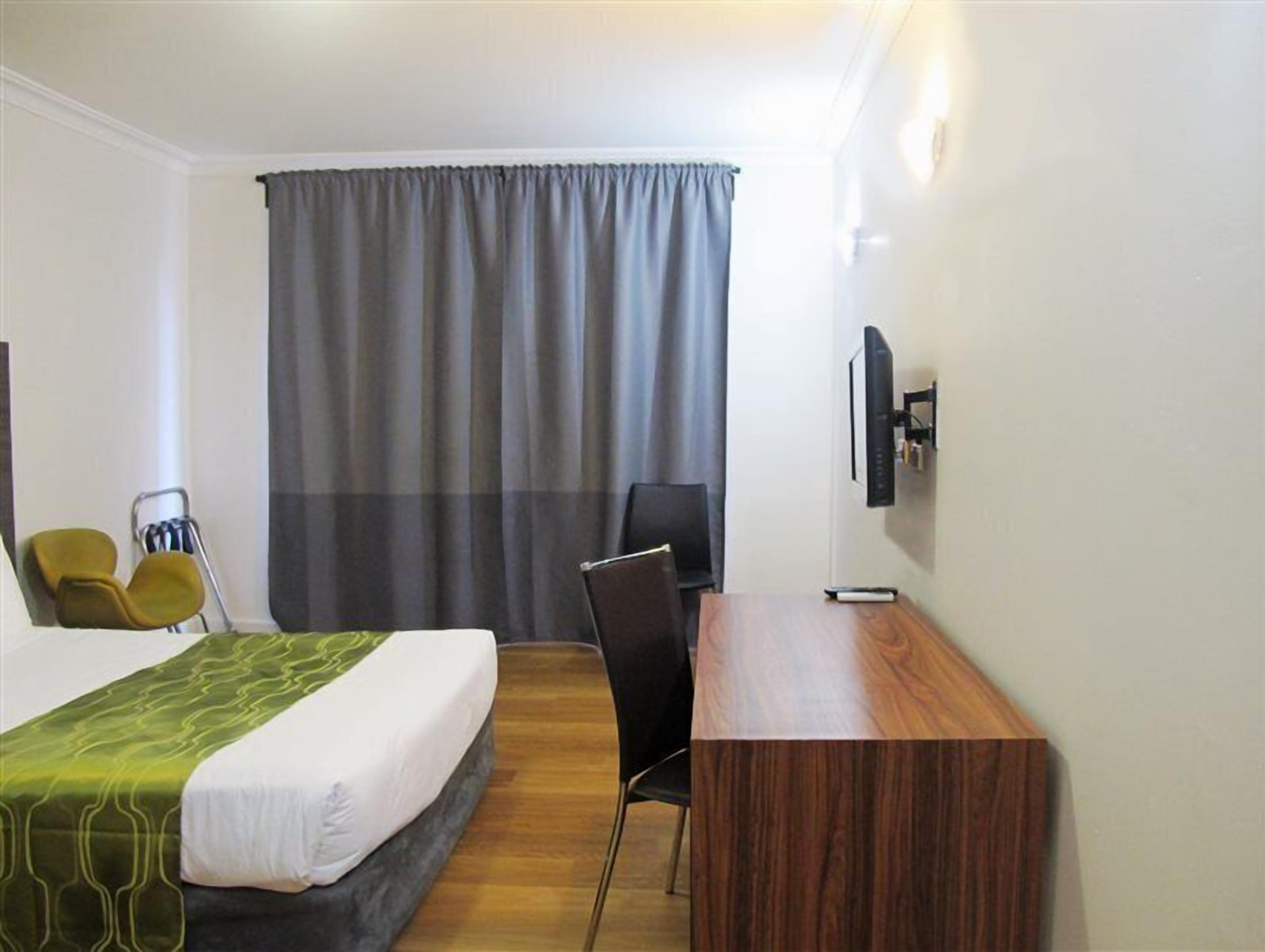 A hotel room with a bed, a desk, a chair, a TV, and a curtain.