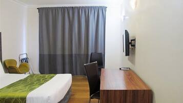 A hotel room with a bed, a desk, a chair, a TV, and a curtain.