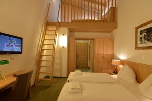 A hotel room with a wooden staircase, a TV, a desk with a chair, two beds with towels, a nightstand with a lamp, and wooden wardrobes. - St Florian Hotel (Kaprun)