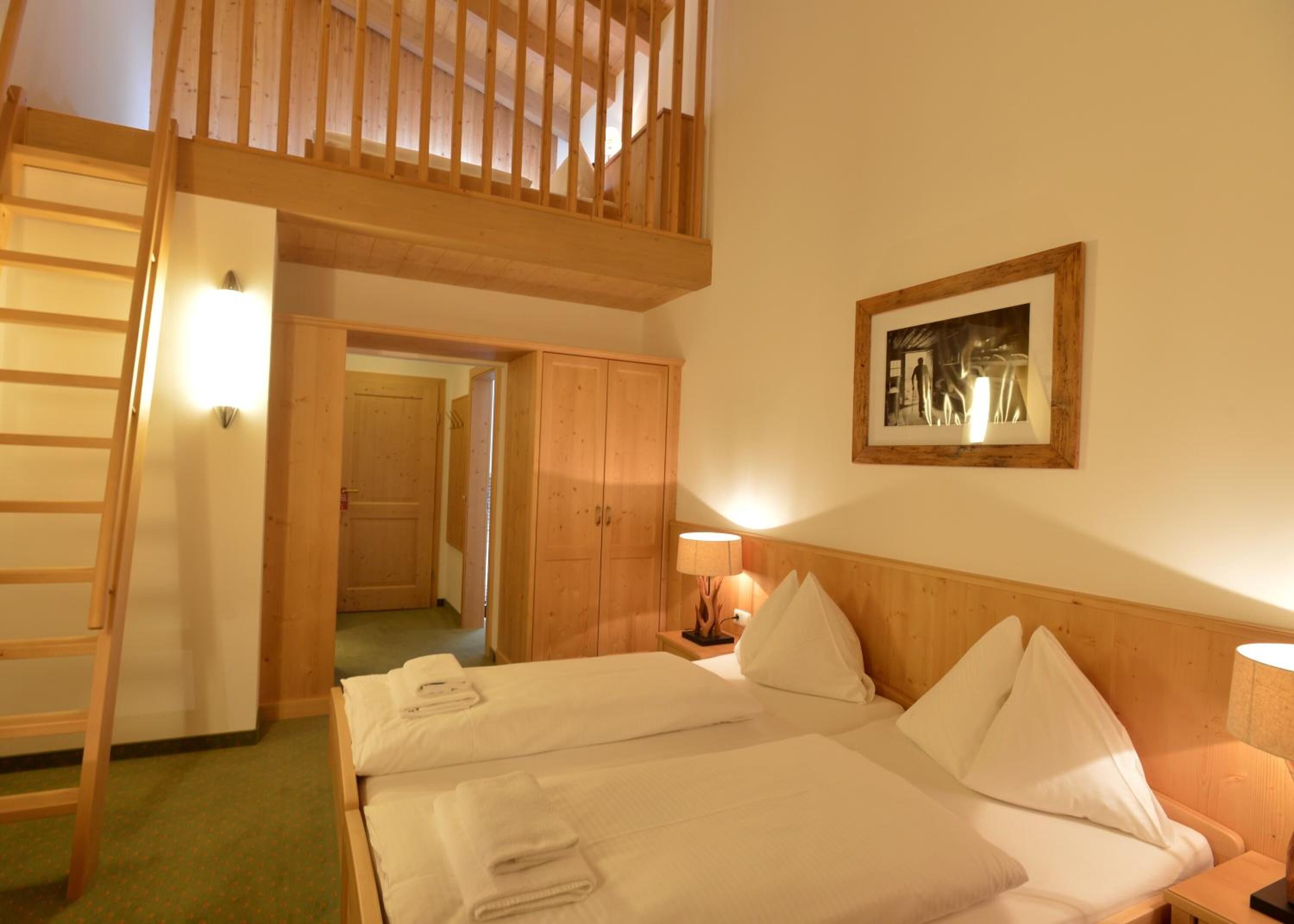 A bedroom with a bunk bed, a wooden ladder, a bedside lamp, and a framed picture on the wall.