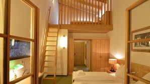A bedroom with a loft bed, a wooden ladder, a desk with a lamp, and a nightstand with a lamp. - St Florian Hotel (Kaprun)
