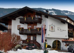A hotel with a white facade, wooden balconies, and a mountain backdrop. - St Florian Hotel (Kaprun)