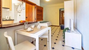 A compact kitchen with a dining area, a white table, and chairs. There is a small refrigerator and a TV on a stand. - Apartments Rio By Garvetur (Loulé)
