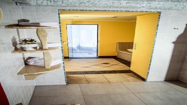 A bathroom with a yellow wall, a sink, and a toilet. There is a towel rack with towels and a small plant. - Pension Alpenrose (Kaprun)