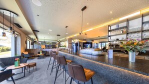 A modern bar area with seating and a counter, featuring a speckled ceiling and shelves with glassware. - Pension Alpenrose (Kaprun)