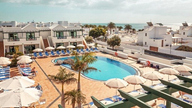 A rooftop pool area with lounge chairs and umbrellas, surrounded by modern buildings with a view of the sea. - Hotel Pocillos Playa (Tías)