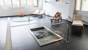 A spa room with a hot tub, two lounge chairs, a massage table, and a large window. - Hotel Pocillos Playa (Tías)