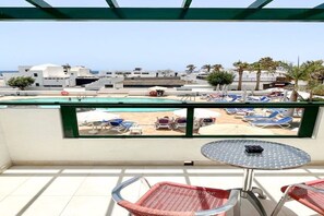 Uma varanda com vista para uma piscina, espreguiçadeiras, uma mesa e um horizonte urbano ao fundo.