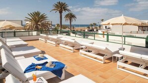 A rooftop terrace with white lounge chairs and umbrellas, overlooking a beach with palm trees. - Hotel Pocillos Playa (Tías)