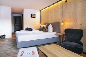 A modern hotel room with a bed, a chair, a small table, and a wooden wall. - Basur (Flirsch)