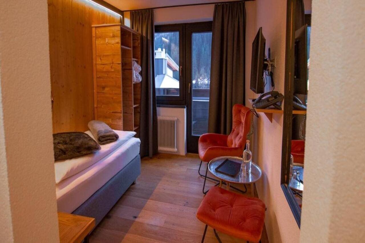 Ein kleines Zimmer mit Schlafsofa, einem kleinen Tisch und einem roten Sessel.