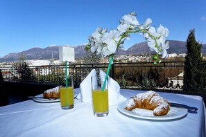 A table with a croissant and juice glasses, a flower arrangement, and a view of mountains and buildings. - Eklips Hotel (Farkë)