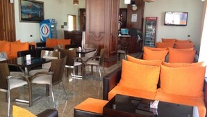 A lobby with orange seating, a Coca-Cola refrigerator, and a television on the wall. - Eklips Hotel (Farkë)