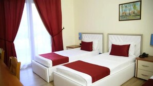 A hotel room with two beds, red curtains, a painting on the wall, and a wooden floor. - Eklips Hotel (Farkë)