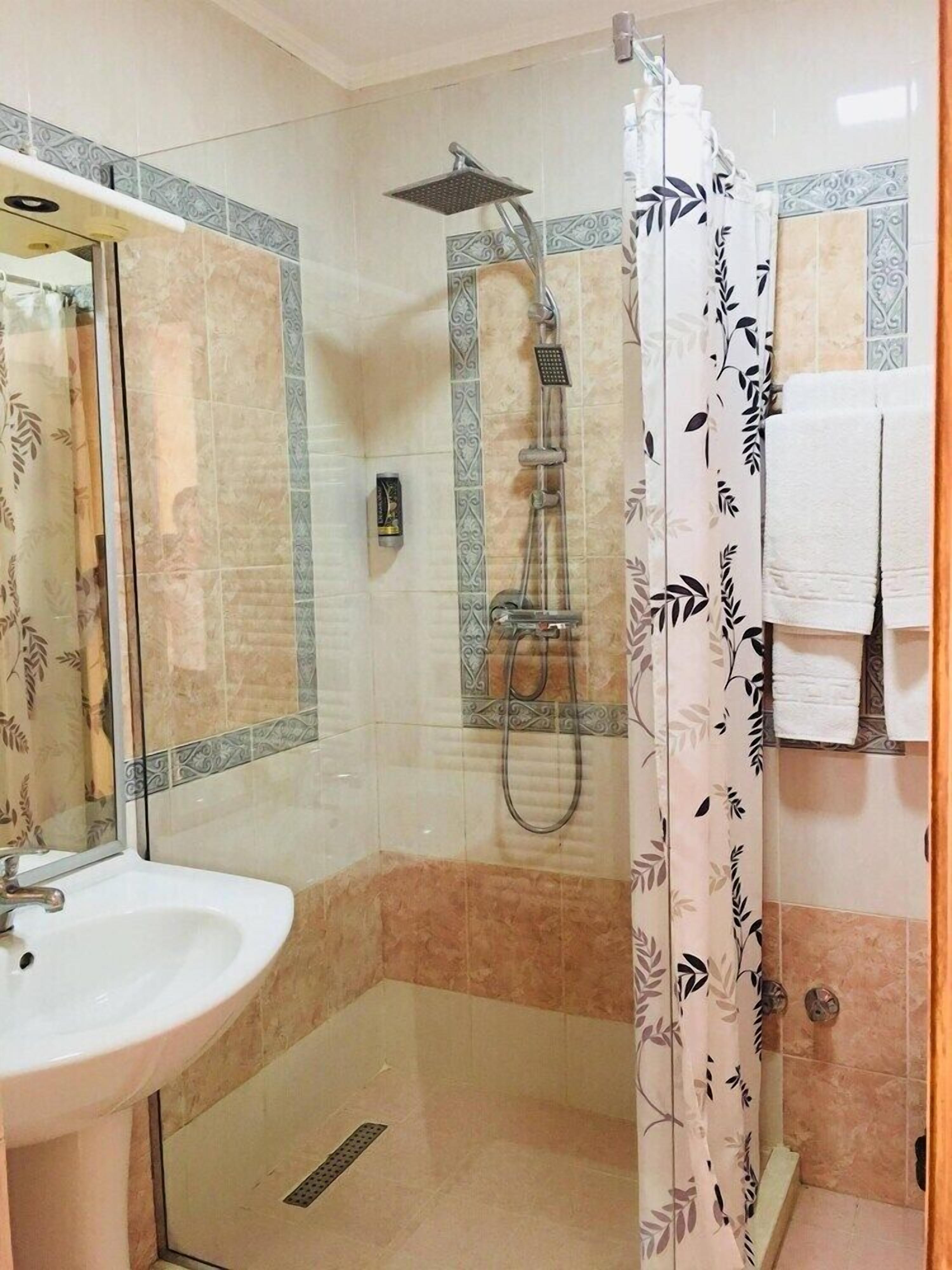 A bathroom with a glass-enclosed shower, a sink, and a mirror.