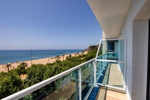 A balcony with a glass railing overlooking a beach with palm trees and the ocean. - Hotel Calella by Beatriz Hoteles (Calella)