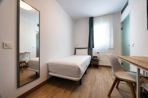 Habitación de hotel con cama, escritorio, silla, espejo y ventana con cortinas.