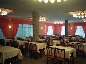 A dining area with multiple tables and chairs, red curtains, and a stone pillar. - Hotel Calella by Beatriz Hoteles (Calella)