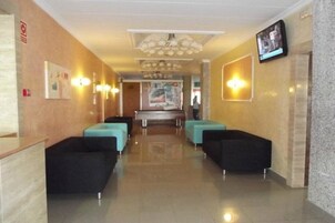Un vestíbulo de hotel con una recepción, zona de estar y una pantalla de televisión.