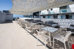 Terraza en la azotea con mobiliario exterior, incluyendo mesas y sillas, y un toldo con diseño que proporciona sombra.