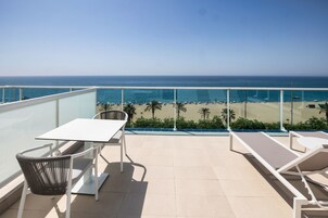 Un balcón con mesa y sillas, con vista a una playa con palmeras y el océano.