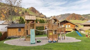 A playground with a slide and climbing structures, surrounded by houses with sloped roofs and solar panels. - Hotel Schneeberger (Wildschönau)