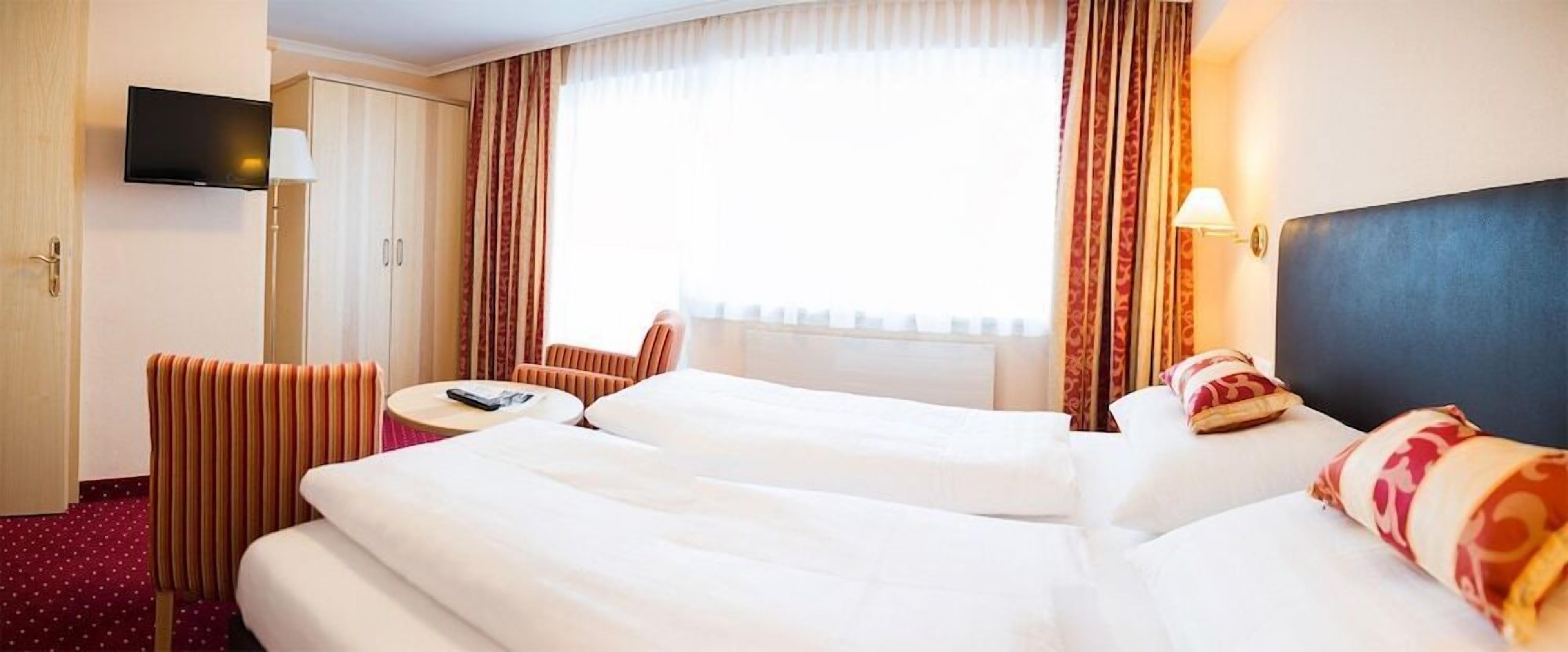 A hotel room with a bed, a desk, a chair, a TV, and curtains.