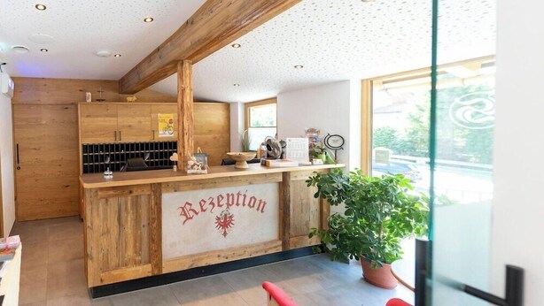 A reception area with a wooden counter, a sign reading "Reception," and a potted plant. - Hotel Schneeberger (Wildschönau)