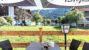 An outdoor seating area with a table and chairs, a wooden fence, and a view of buildings and trees in the background. - Hotel Schneeberger (Wildschönau)
