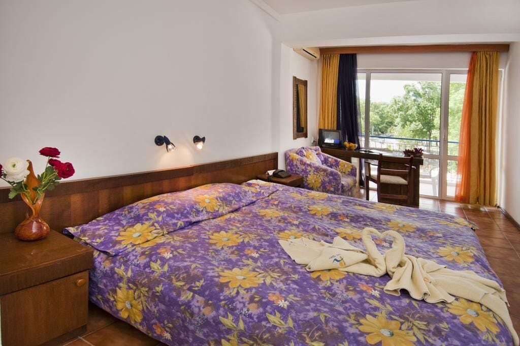 A hotel room with a large bed, a desk, and a balcony with curtains.