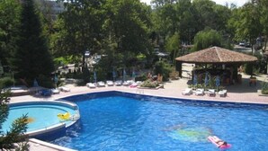 Una piscina con sillas de descanso y sombrillas, rodeada de árboles y una zona cubierta.