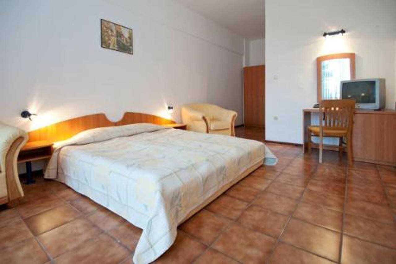 Ein Schlafzimmer mit einem Bett, zwei Stühlen, einem Schreibtisch mit Computer und einem Fernseher.