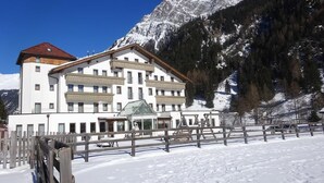 A large, multi-story hotel with a white facade and a red roof, surrounded by snow-covered mountains and a wooden fence. - Hotel Tia Monte (Kaunertal)