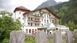 A multi-story hotel with balconies, a glass conservatory, and a mountainous backdrop. - Hotel Tia Monte (Kaunertal)
