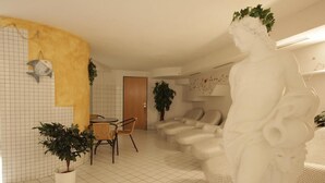 A living room with a white tiled floor, a sofa set, a dining table with chairs, a potted plant, and a white statue. - Hotel Tia Monte (Kaunertal)