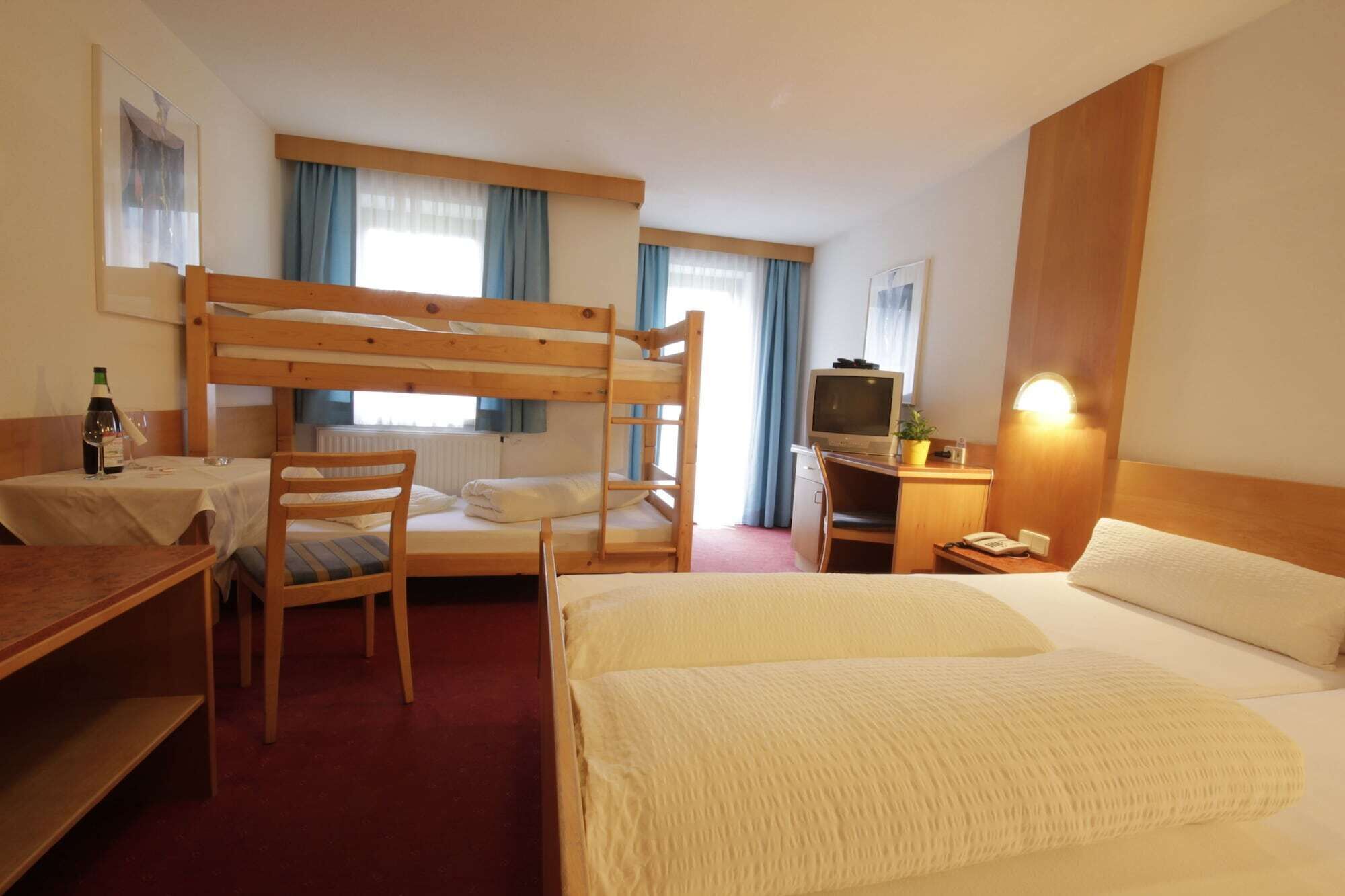 A hotel room with bunk beds, a desk with a chair, a television, and a bedside table with a lamp.