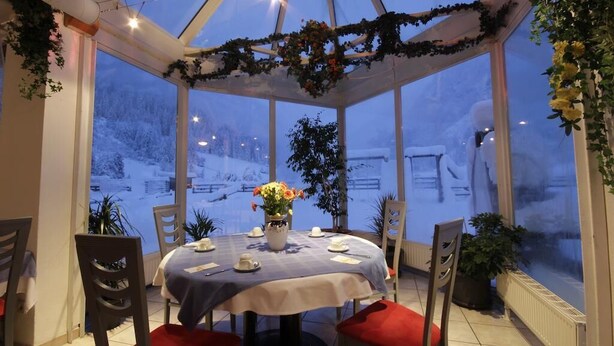 A conservatory with a table set for two, surrounded by chairs, and a vase of flowers on the table. - Hotel Tia Monte (Kaunertal)